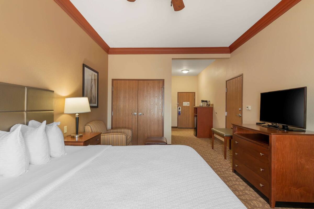 A hotel room with a large bed, a desk with a lamp, a television, a wardrobe, and a chair.