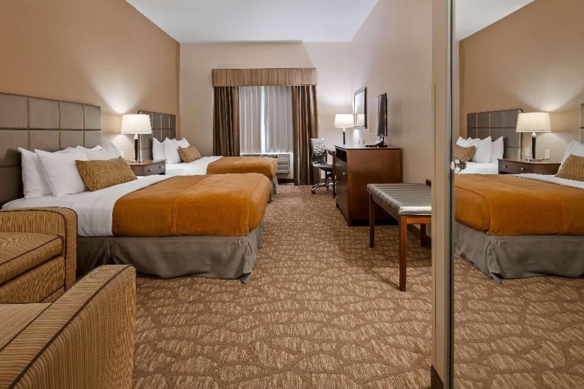 A hotel room with two beds, a desk, a chair, and a mirror.