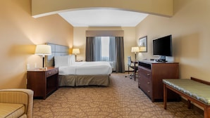 A hotel room with a bed, desk, chair, TV, and a small seating area.
