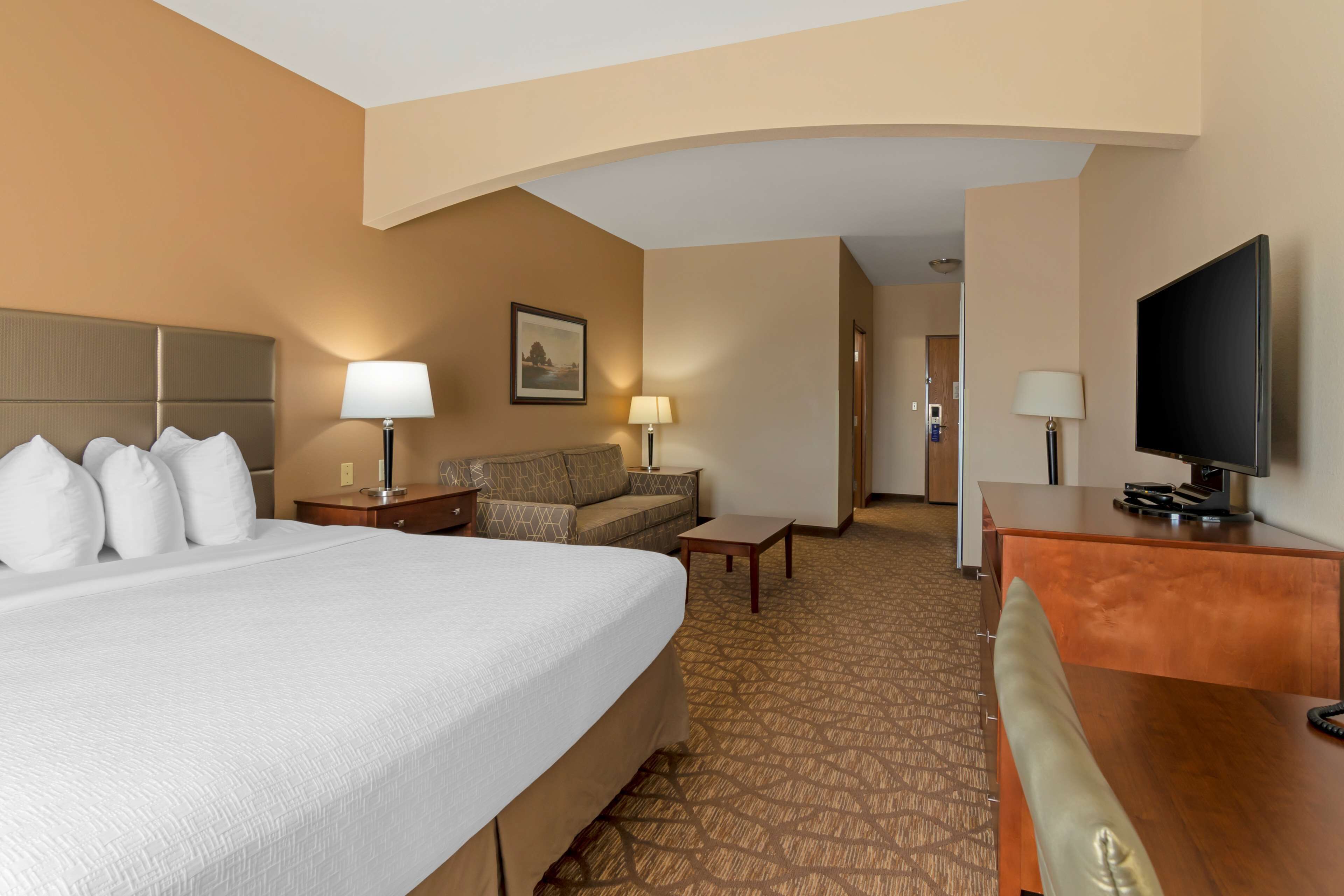 A hotel room with a large bed, a sofa, a desk, a television, and two lamps.