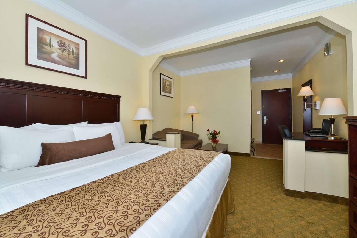 Ein Hotelzimmer mit einem großen Bett, einem Schreibtisch, einem Stuhl, einer Lampe und einem gerahmten Bild an der Wand.