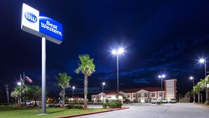 A Best Western hotel at night with a well-lit entrance, palm trees, and a parking lot. - Best Western Lone Star Inn (Edna)