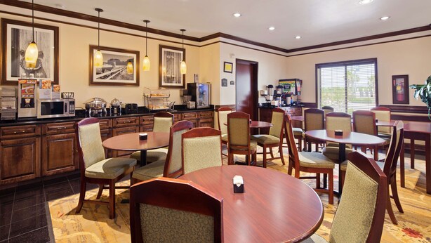 A hotel dining area with round tables and chairs, a buffet counter, and framed pictures on the walls. - Best Western Lone Star Inn (Edna)