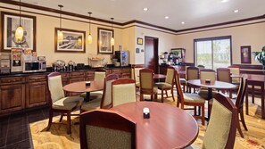 Une salle à manger d’hôtel avec des tables et des chaises rondes, un buffet et des tableaux encadrés aux murs.