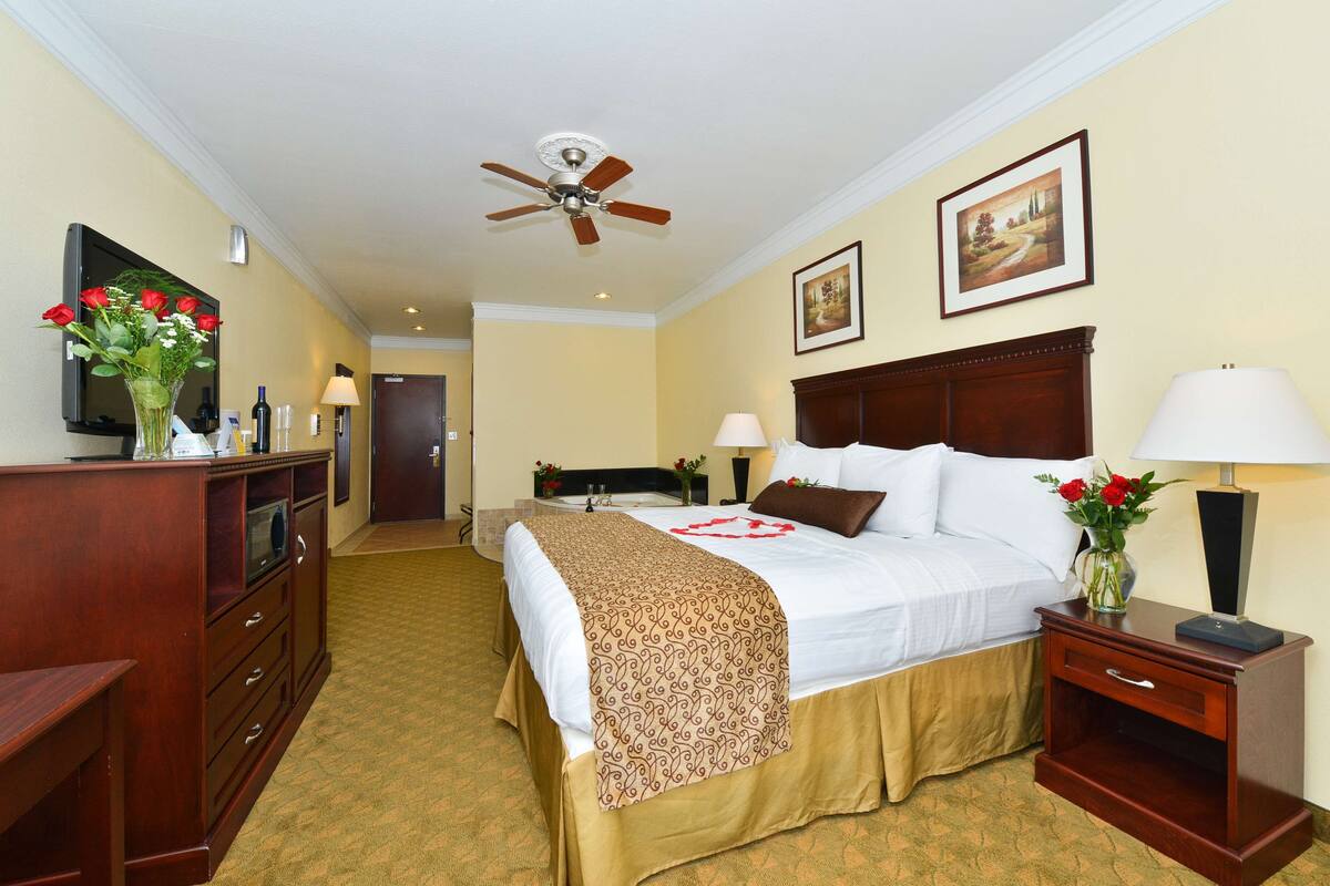 Ein Hotelzimmer mit Bett, Nachttischen, Schreibtisch, Deckenventilator und einem Gemälde an der Wand.