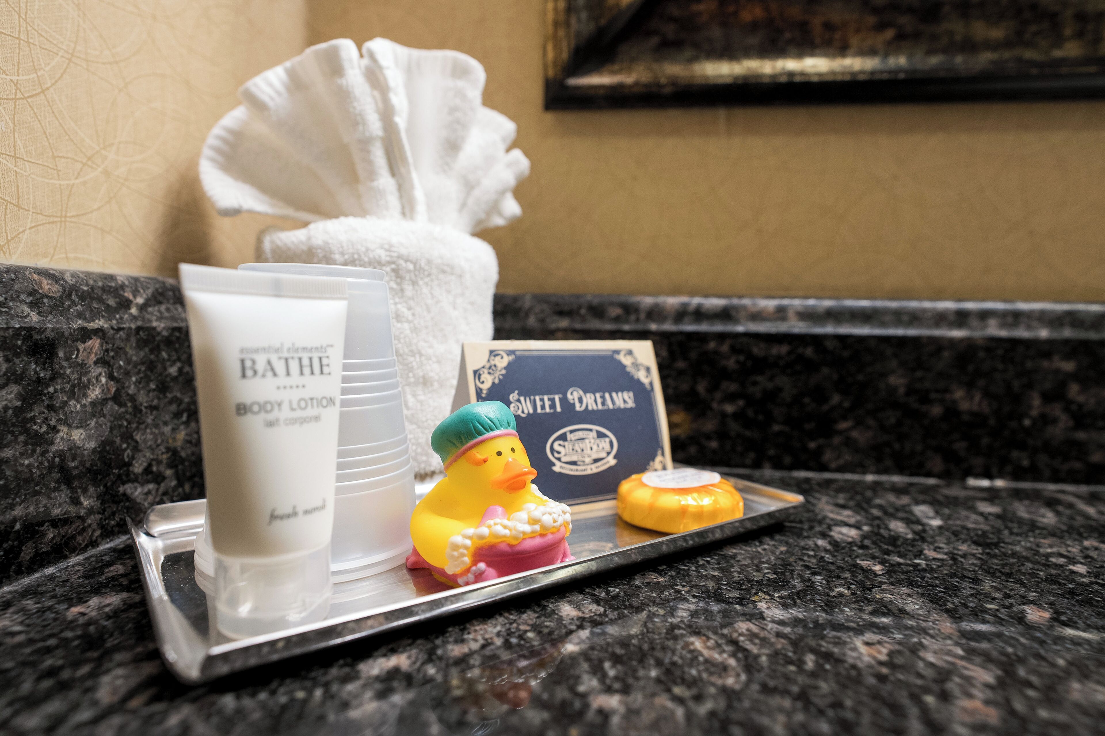 Toiletries on a tray, including a body lotion, a duck figurine, and a sweet dreams card.