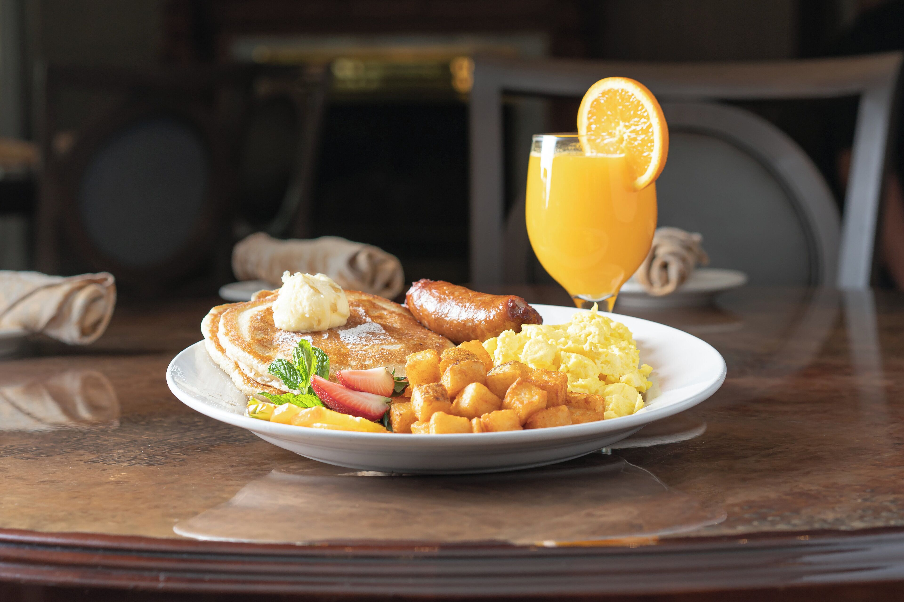 A breakfast plate with pancakes, sausage, scrambled eggs, and toast, accompanied by a glass of orange juice.