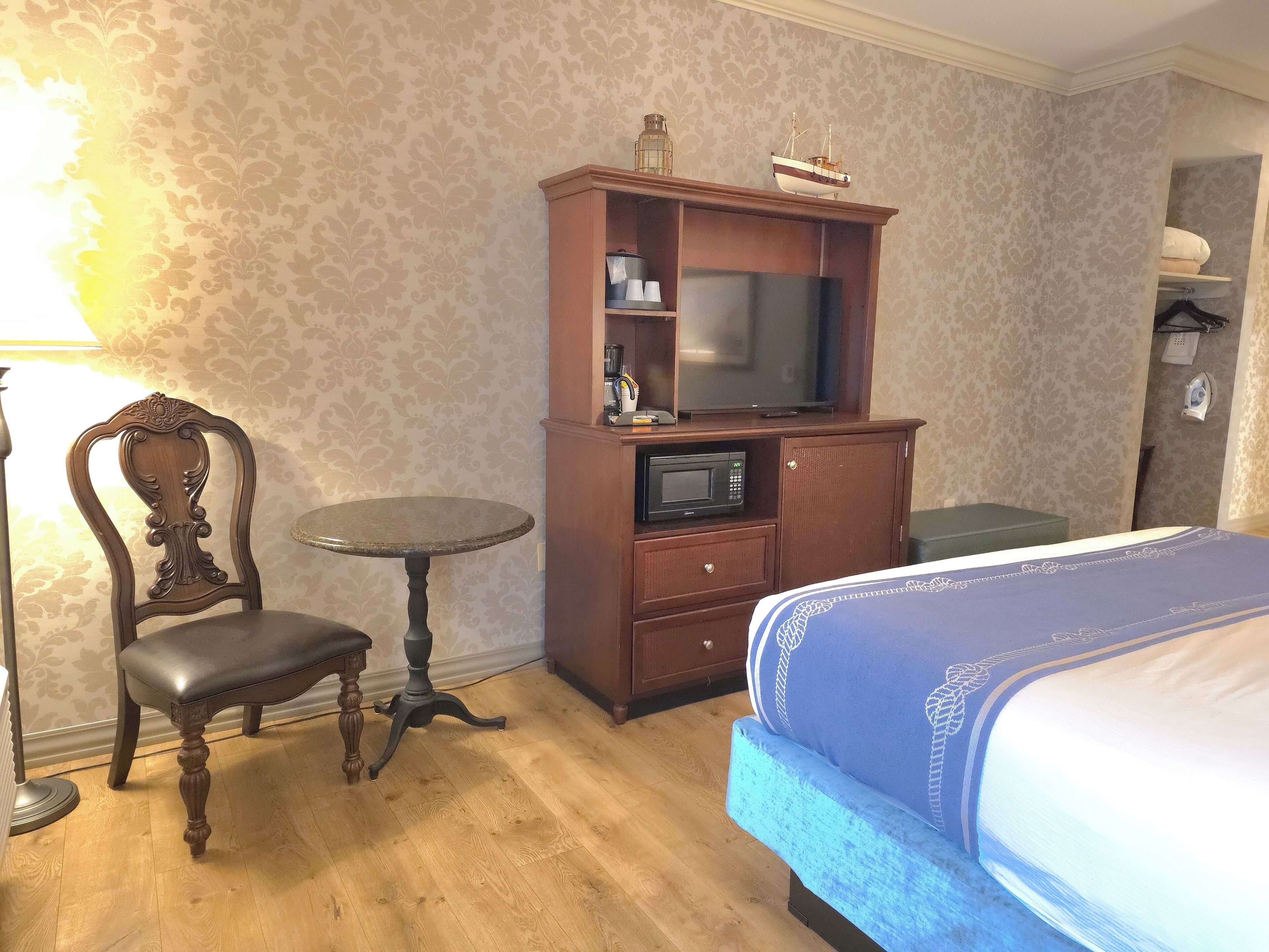 Quarto de hotel com uma cama, um armário de madeira com televisão, uma cadeira e uma mesinha.