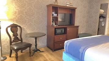 Quarto de hotel com uma cama, um armário de madeira com televisão, uma cadeira e uma mesinha.