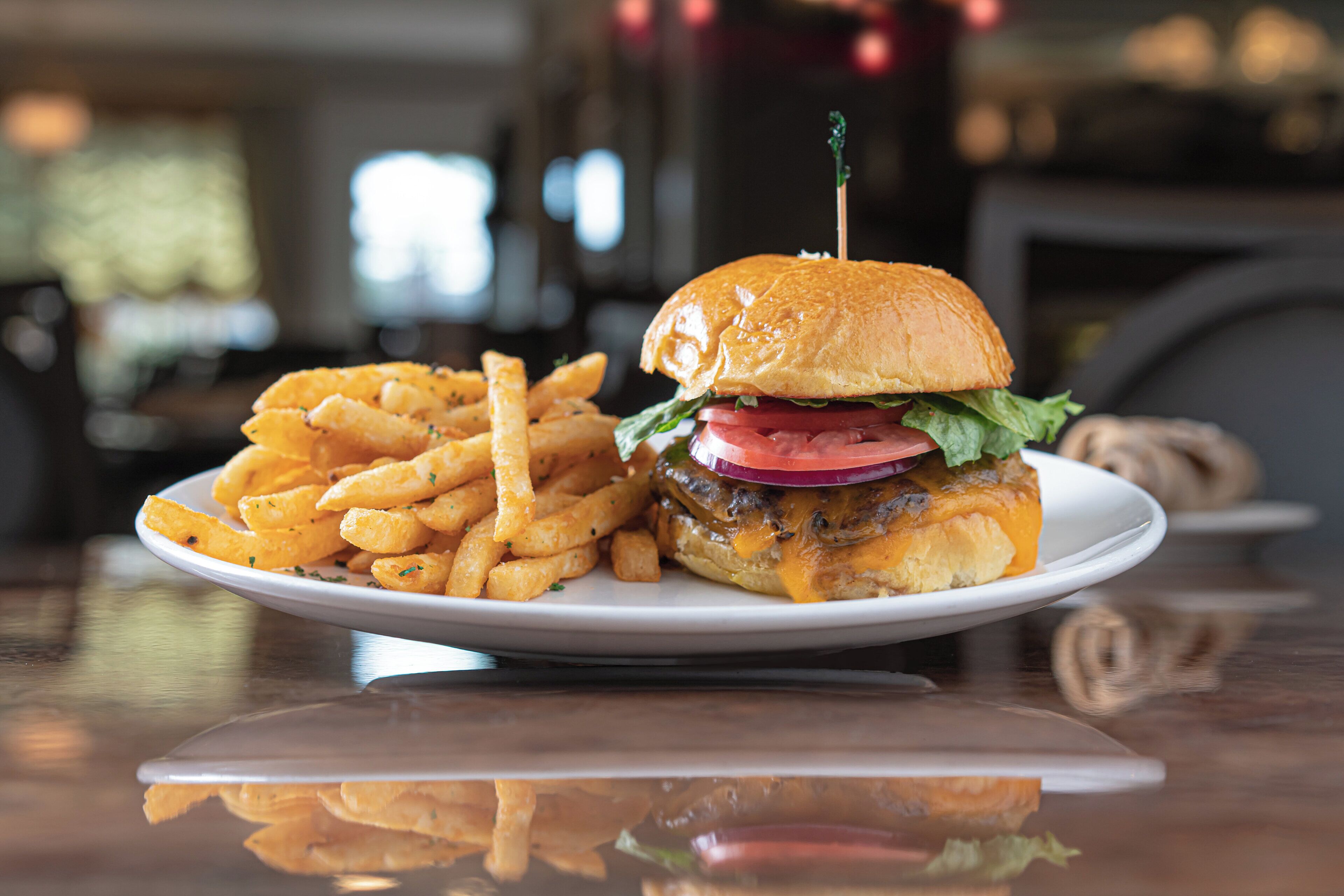 A plate with a burger and fries on a reflective surface.