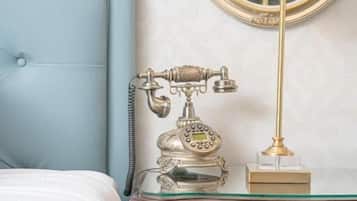 Uma cama com cabeceira azul, uma mesa de cabeceira de madeira com abajur, telefone e espelho.