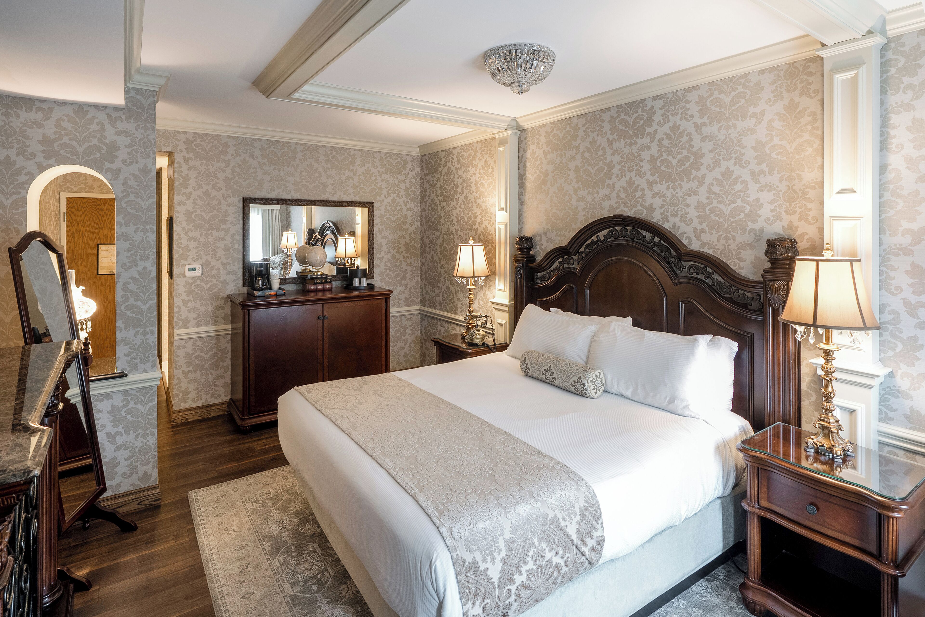 Une chambre d’hôtel avec un grand lit, une tête de lit en bois, une commode, un miroir et deux lampes de chevet.