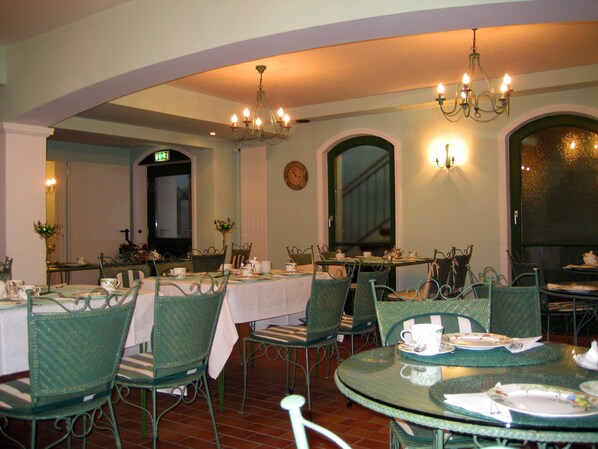 A dining area with round tables, green chairs, and chandeliers.