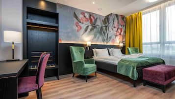 A hotel room with a bed, two chairs, a desk, and a large window with curtains.
