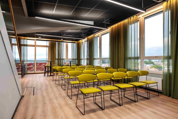 A conference room with yellow chairs arranged in rows, large windows with curtains, and a view of the cityscape.