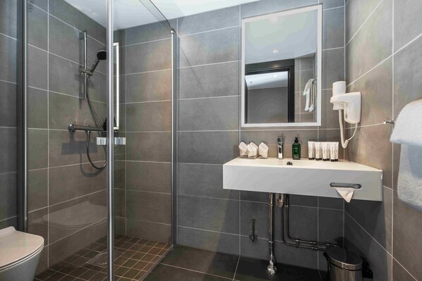 Un baño moderno con ducha envuelta en vidrio, un lavabo blanco con artículos de aseo y un espejo sobre él.