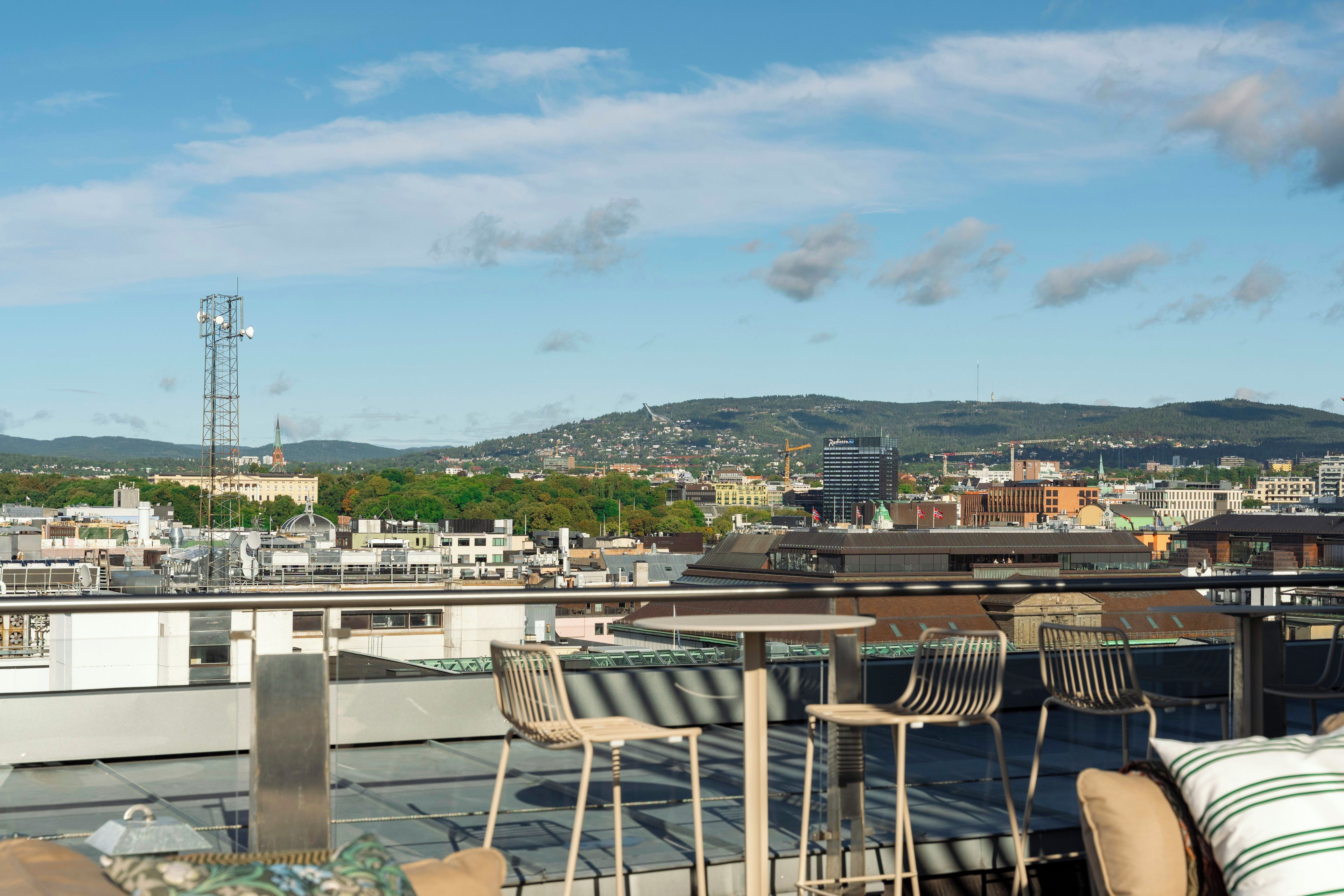 Una terraza en la azotea con vistas a un paisaje urbano, que incluye edificios y una cadena montañosa distante.