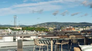 Una terraza en la azotea con vistas a un paisaje urbano, que incluye edificios y una cadena montañosa distante.