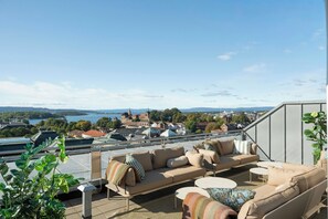 A terrace with outdoor furniture, a view of a cityscape, and a body of water in the distance.