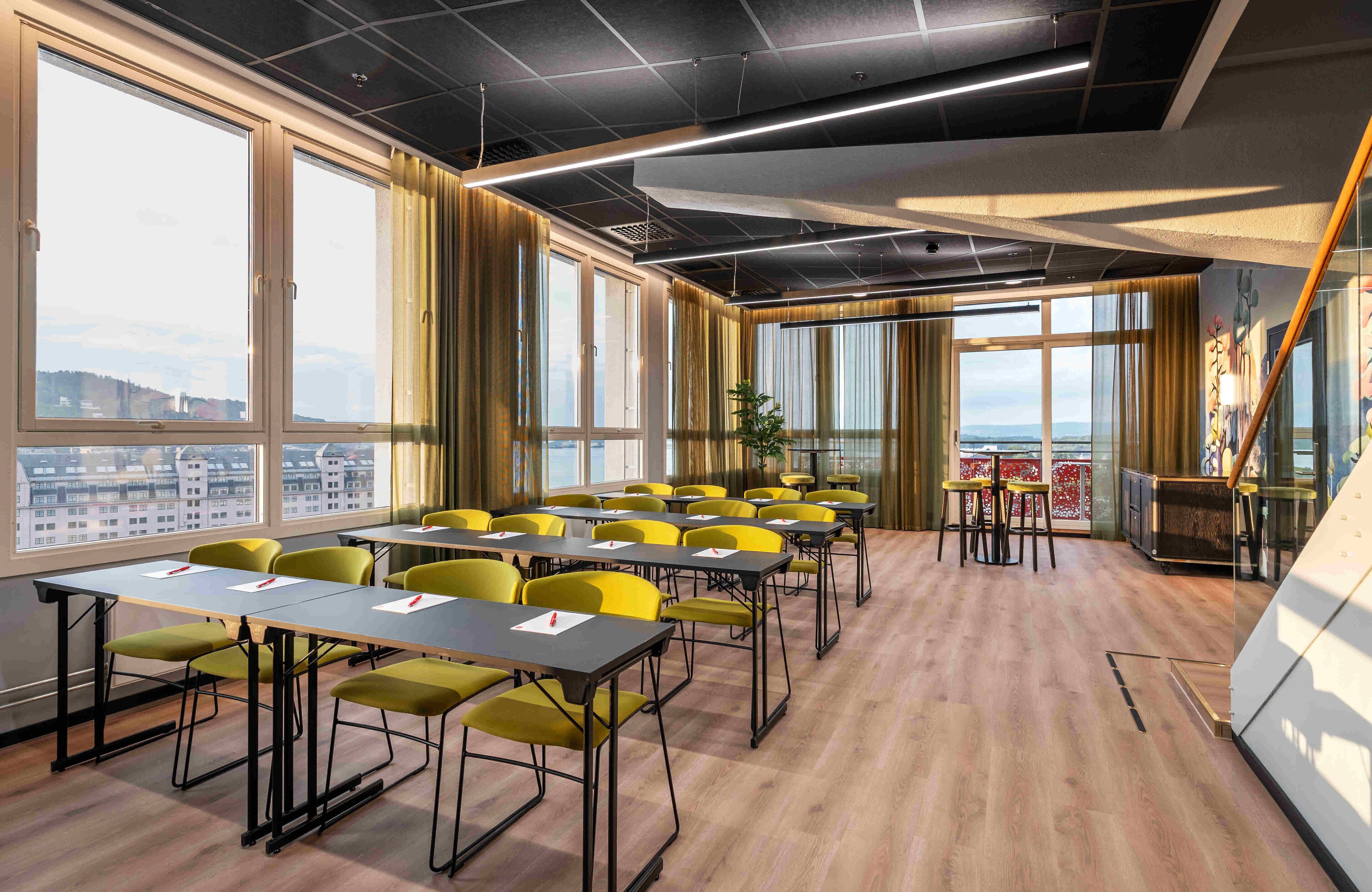 Una sala conferenze con tavoli e sedie, ampie finestre e vista sulla città.