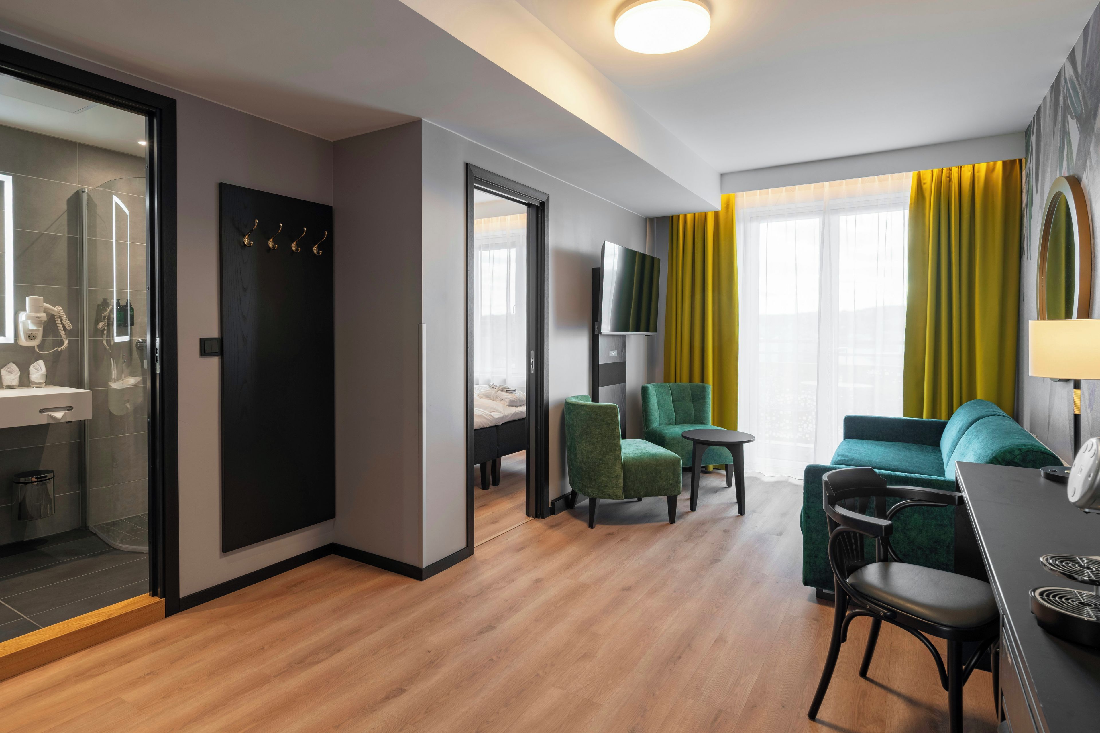 A modern hotel room with a shower, a bed, a TV, a dining area, and a seating space.