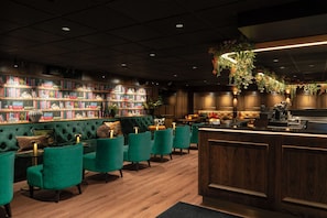 A bar area with a wooden counter, green upholstered chairs, and a bookshelf filled with books. - Thon Hotel Panorama (Oslo)