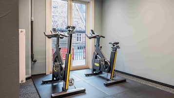 A gym with three stationary bikes, a door, and a window with a view of buildings.