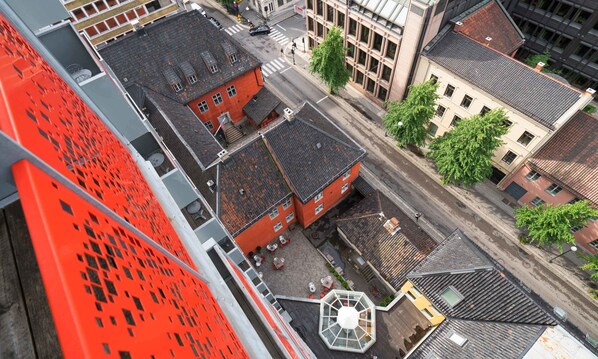 Un edificio de gran altura con fachada roja y una terraza en la azotea con asientos al aire libre.