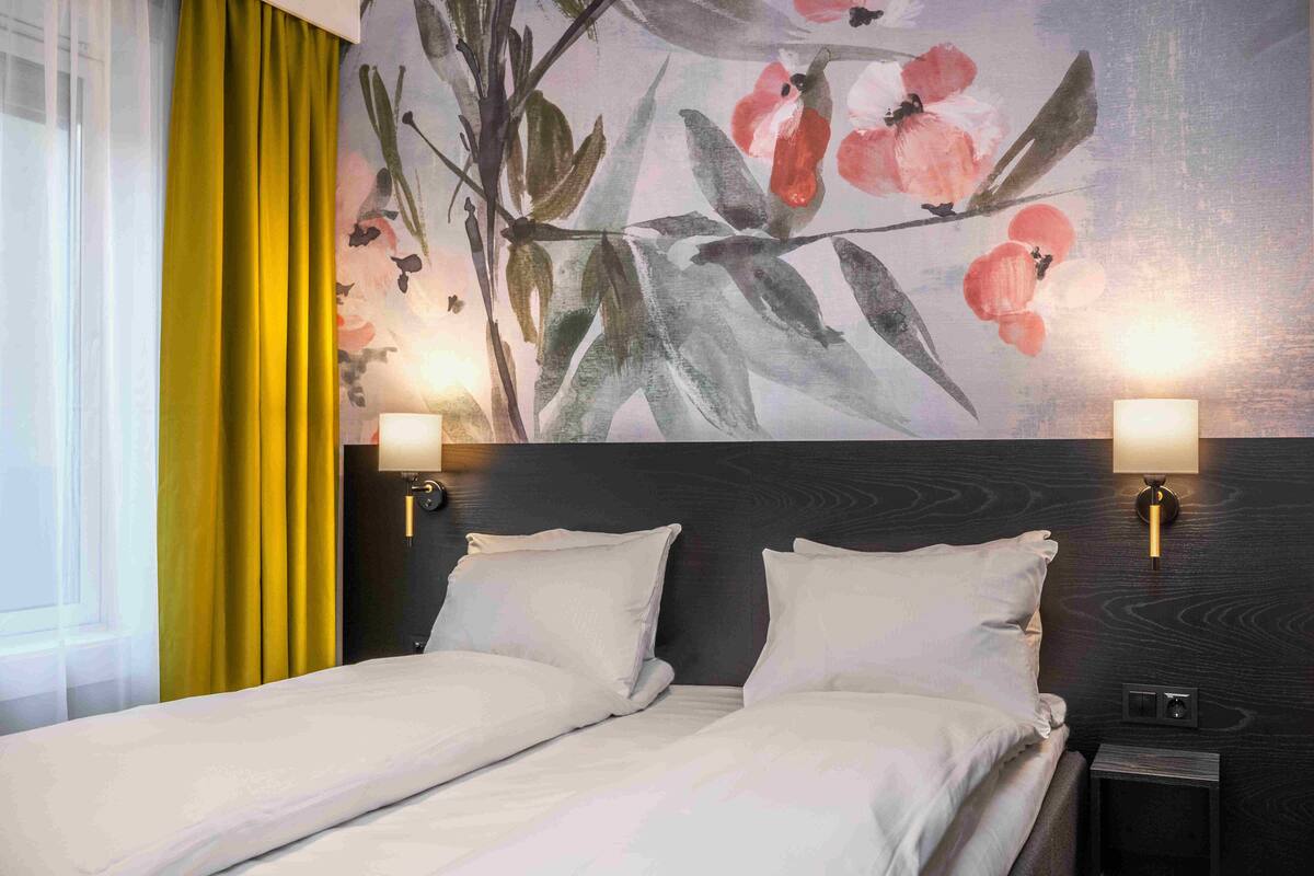 A hotel room with a bed, two bedside lamps, a nightstand, and a floral wall mural.