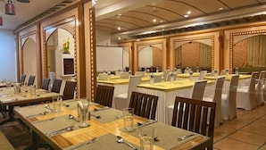 A banquet hall with multiple tables set for dining, equipped with chairs, place settings, and water glasses. - Silicrest Hotel (Bengaluru)
