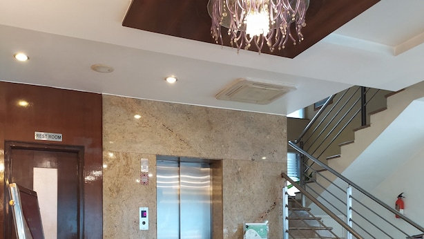 A modern lobby with a marble floor, a chandelier, an elevator, a staircase, and potted plants. - Silicrest Hotel (Bengaluru)