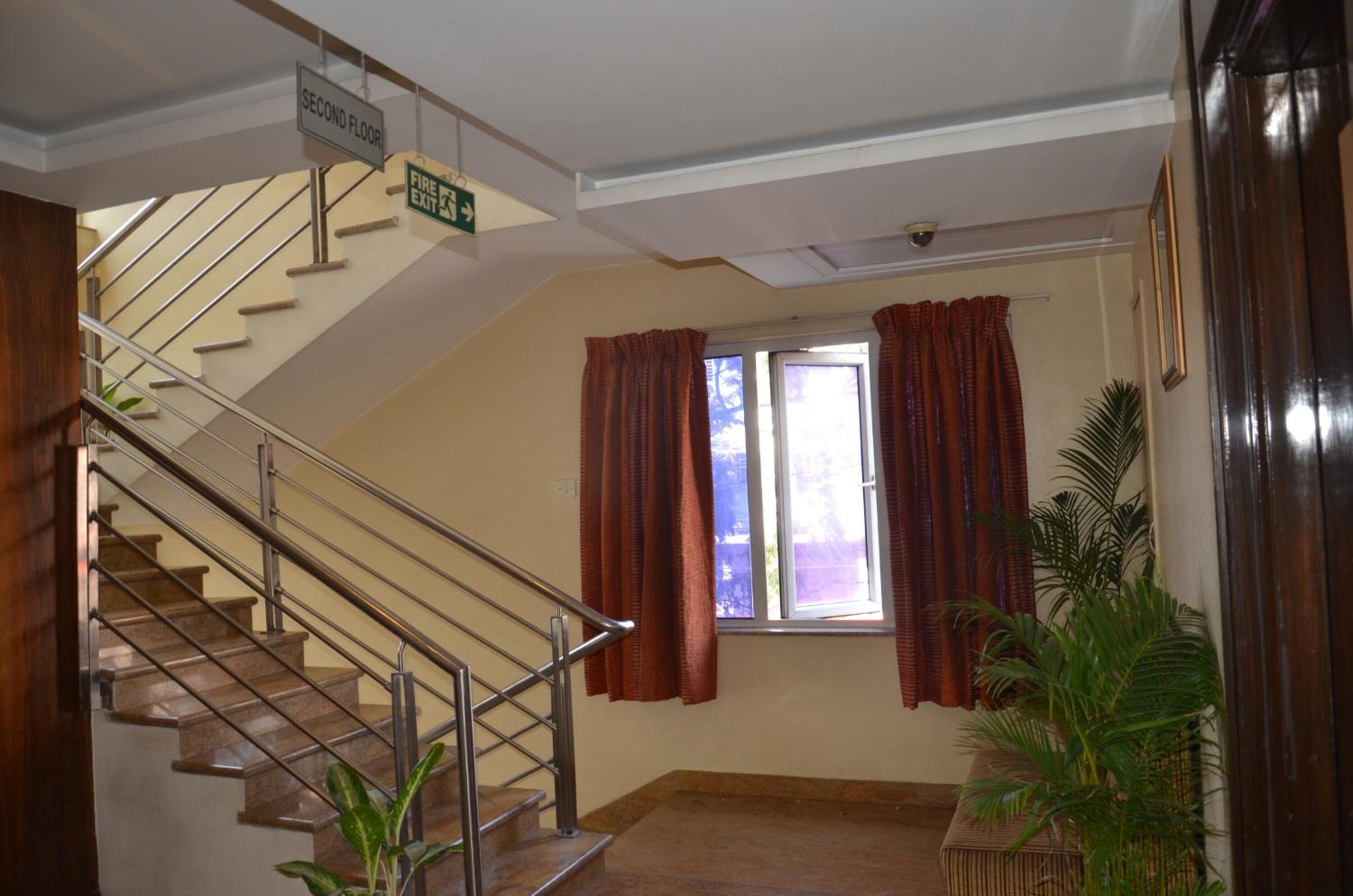 Una escalera con barandilla metálica que lleva al segundo piso, una ventana con cortinas y una planta en el suelo.