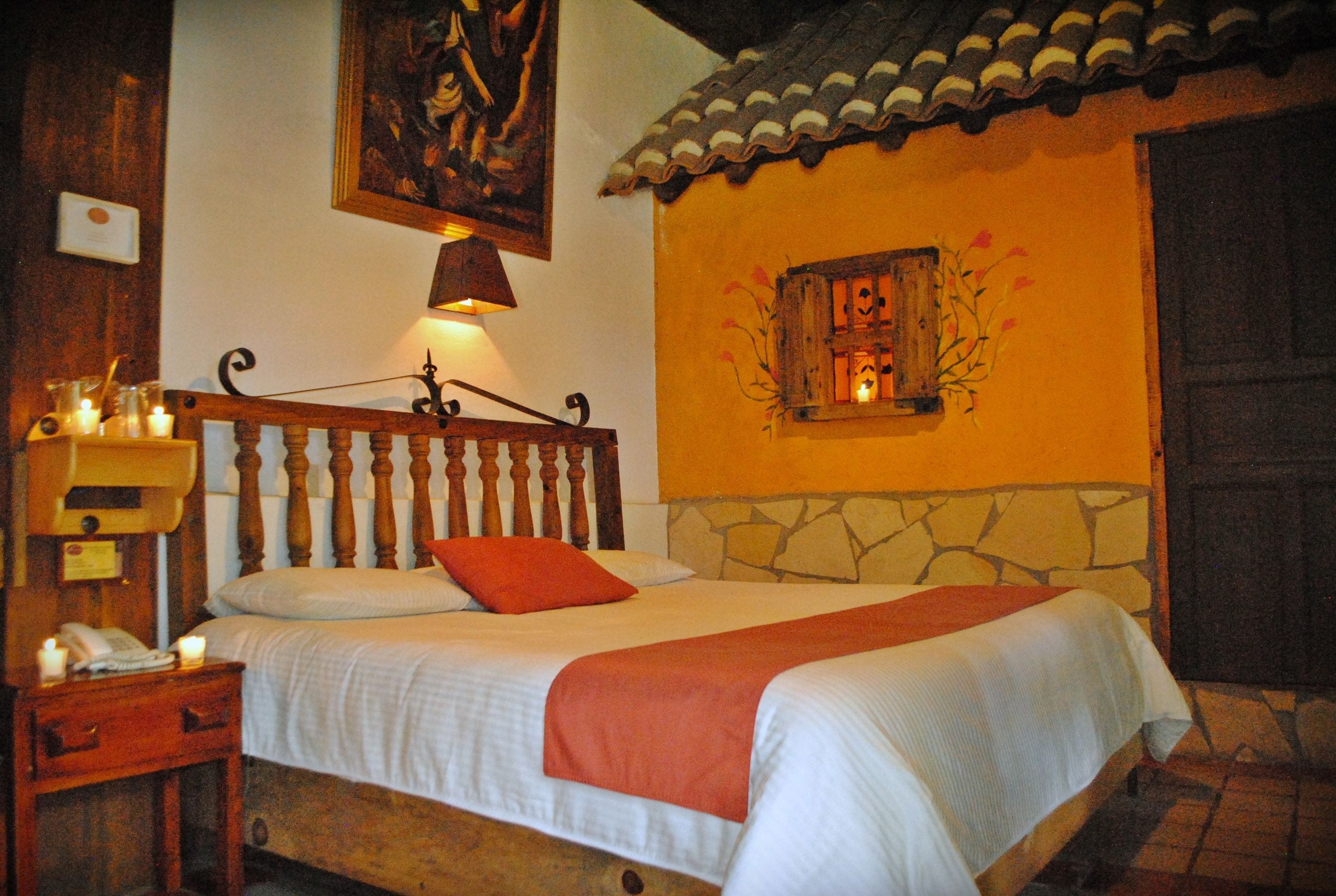 A bedroom with a wooden bed, a nightstand with a lamp, and a painting on the wall.