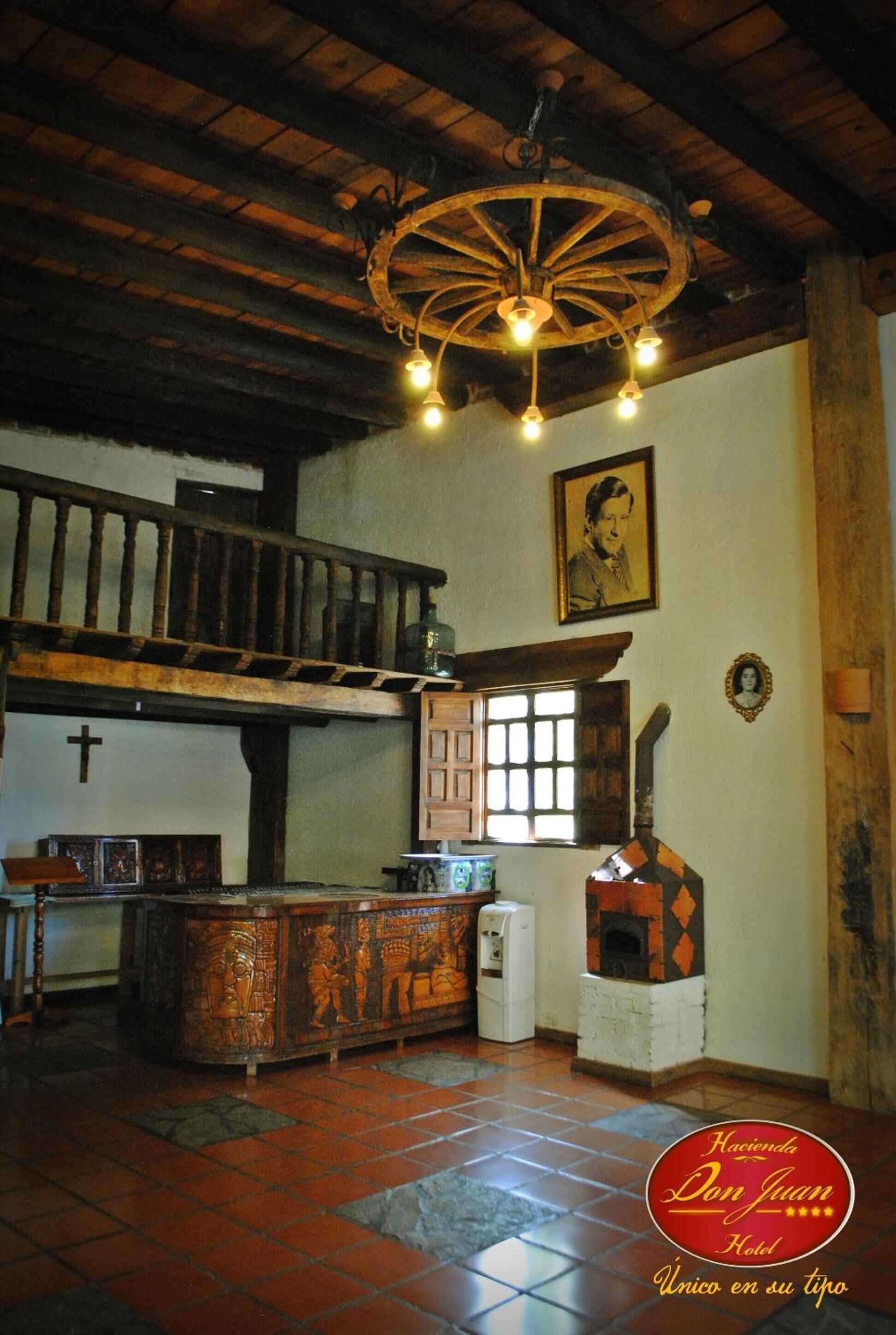 A rustic interior with a wooden ceiling, a staircase, a fireplace, and a cross on the wall.