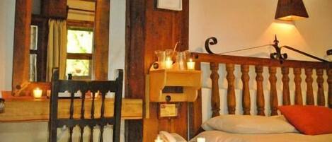 A cozy room with a wooden bed, a chair, a small table with candles, and a painting on the wall.