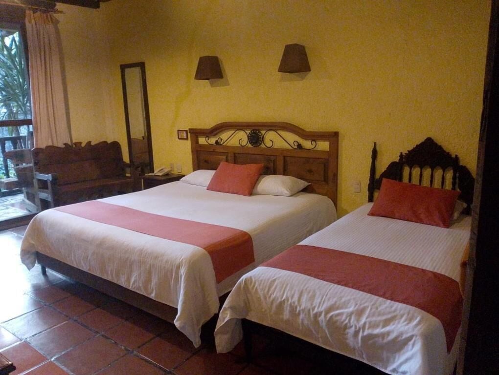 Une chambre d’hôtel avec deux lits, une tête de lit en bois, une table de chevet, un miroir et une fenêtre avec des rideaux.