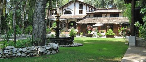 A hotel with a garden featuring a fountain, stone wall, and potted plants.