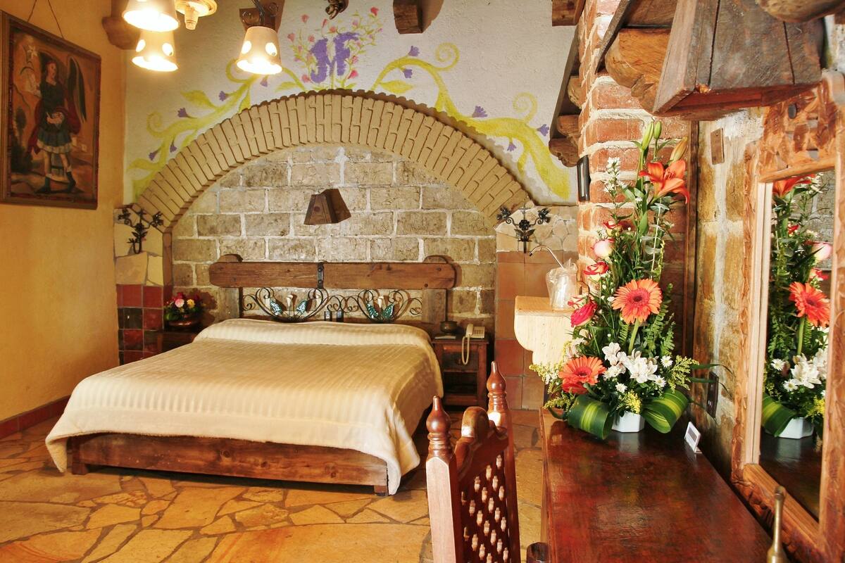 A room with a stone fireplace, a wooden bed, and a flower arrangement.