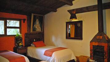 A room with two beds, a wooden ceiling, a fireplace, and a window with a view of trees.