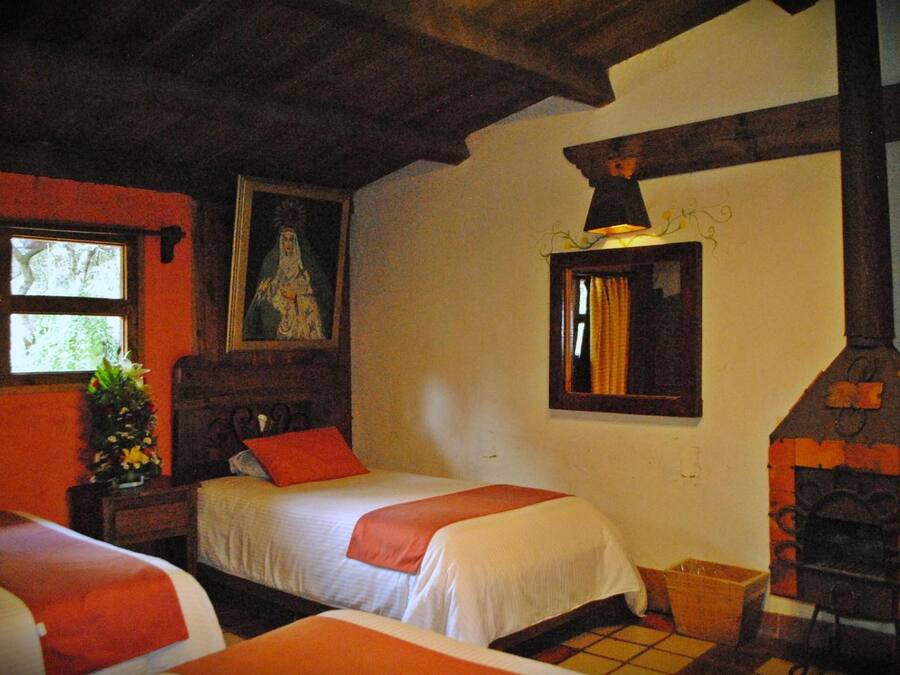A room with two beds, a wooden ceiling, a fireplace, and a window with a view of trees.