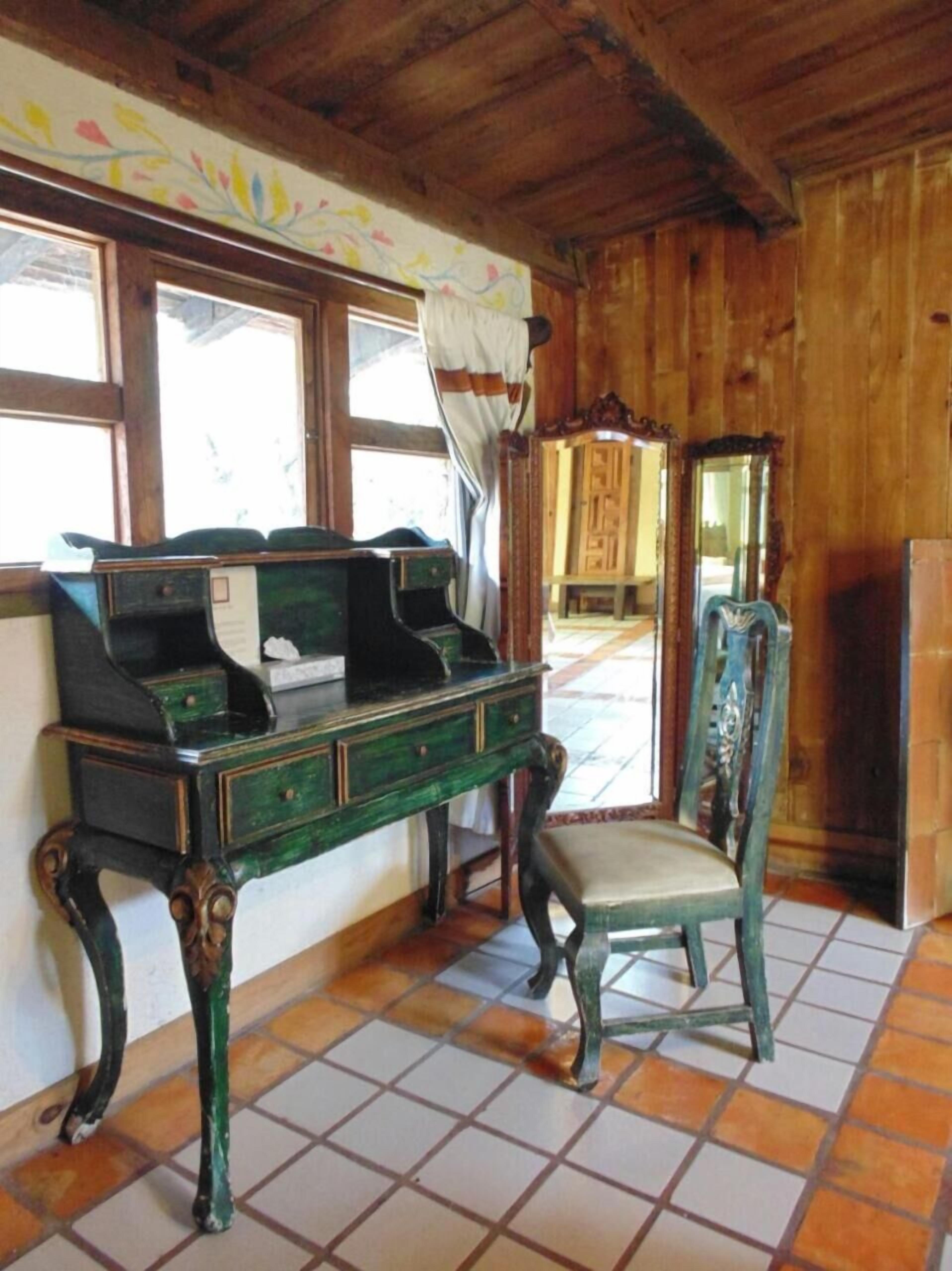 Een kamer met een houten bureau, een stoel, een spiegel en een raam met gordijnen.