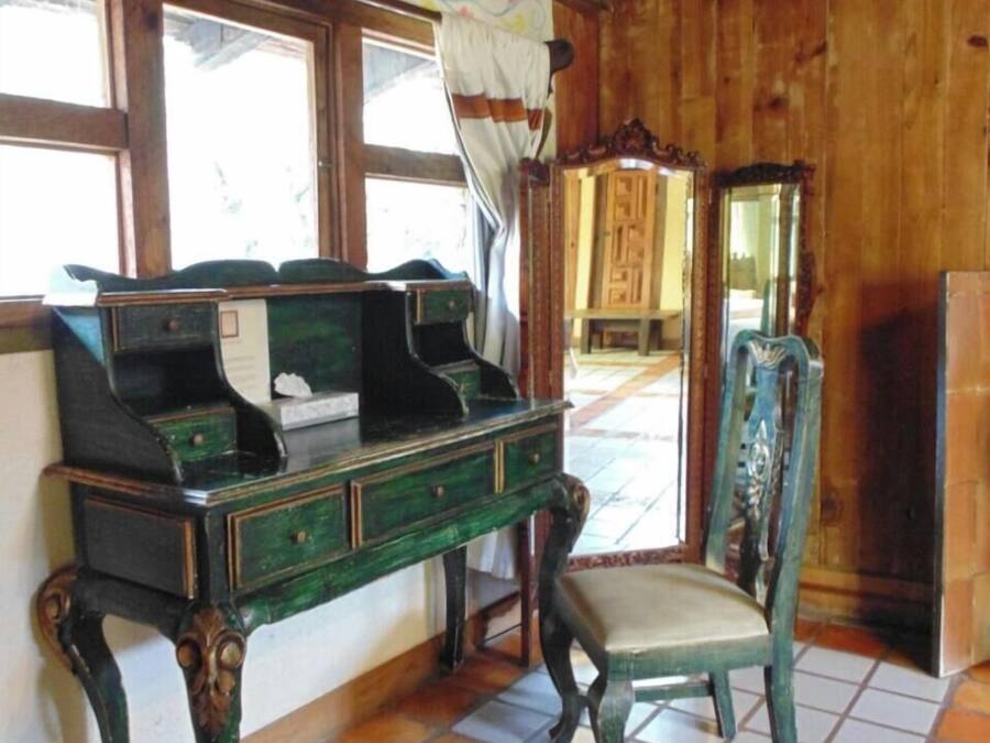 Una stanza con una scrivania in legno, una sedia, uno specchio e una finestra con tende.