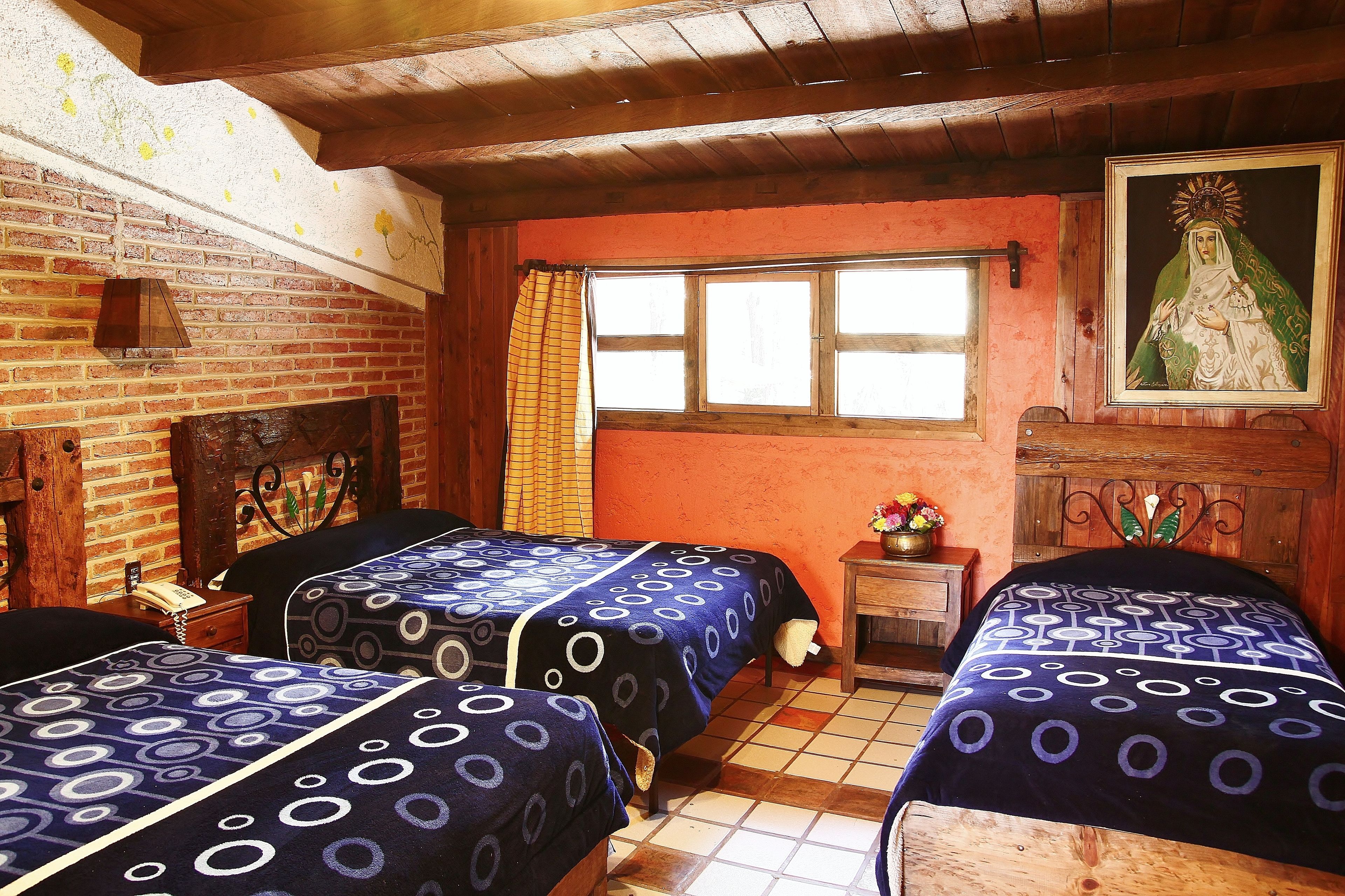 A room with two beds, a wooden ceiling, a brick wall, a window, and a painting.