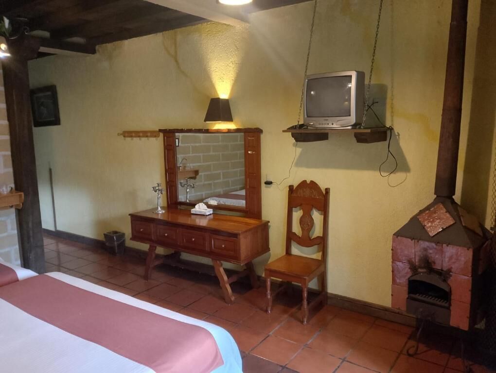 A room with a bed, wooden dresser, chair, television, and a wood-burning stove.