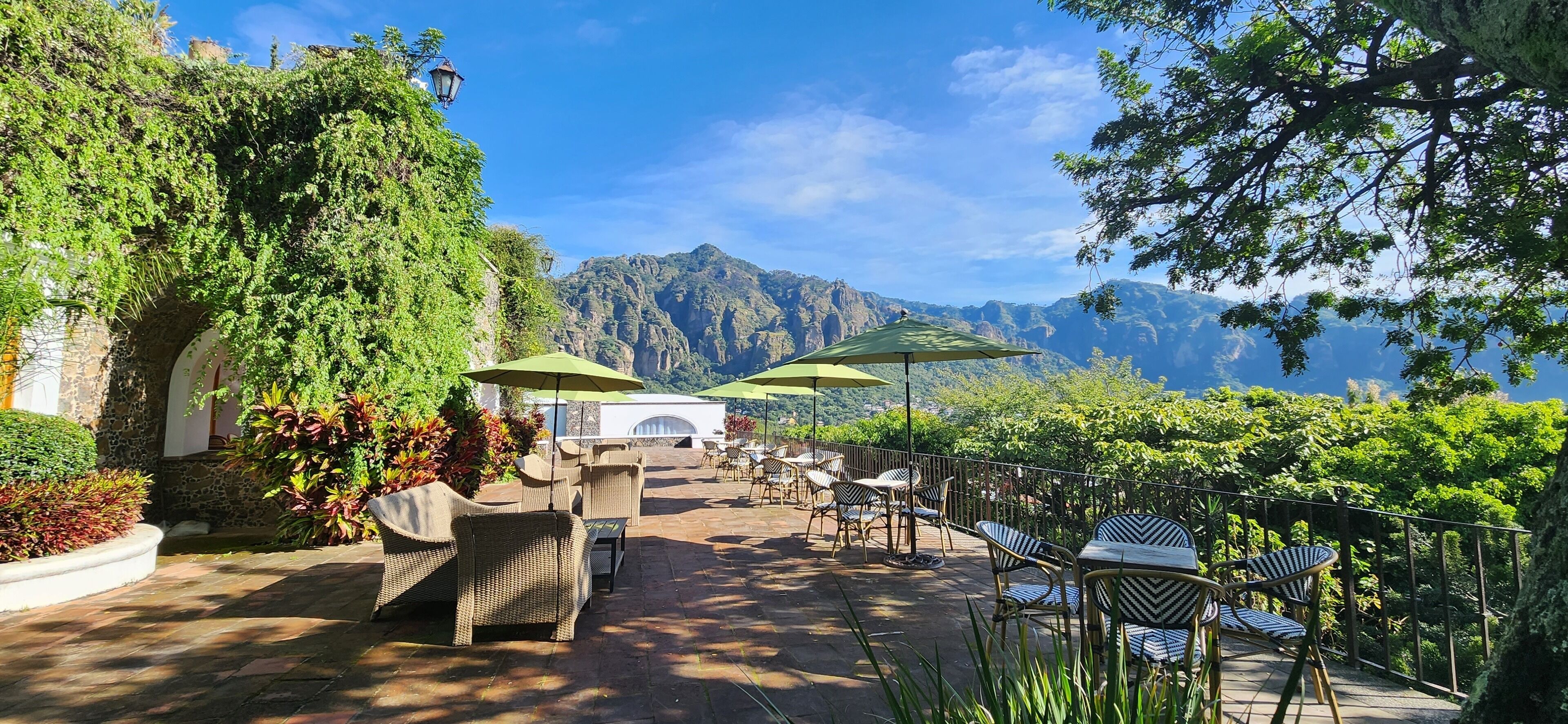Une terrasse extérieure aménagée avec des meubles en osier et des parasols, offrant une vue sur un paysage montagneux.