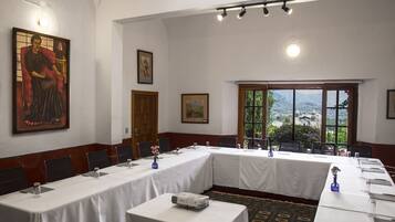 A conference room with long tables, chairs, a projector, and framed artwork on the walls.