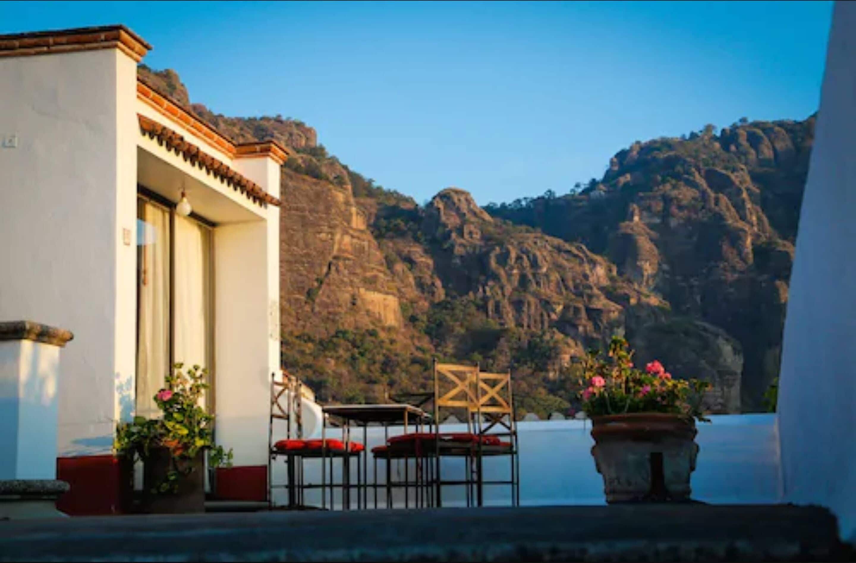 Un bâtiment situé sur la côte, doté d’une terrasse, d’une table et de chaises, et offrant une vue sur une étendue d’eau et des falaises rocheuses.