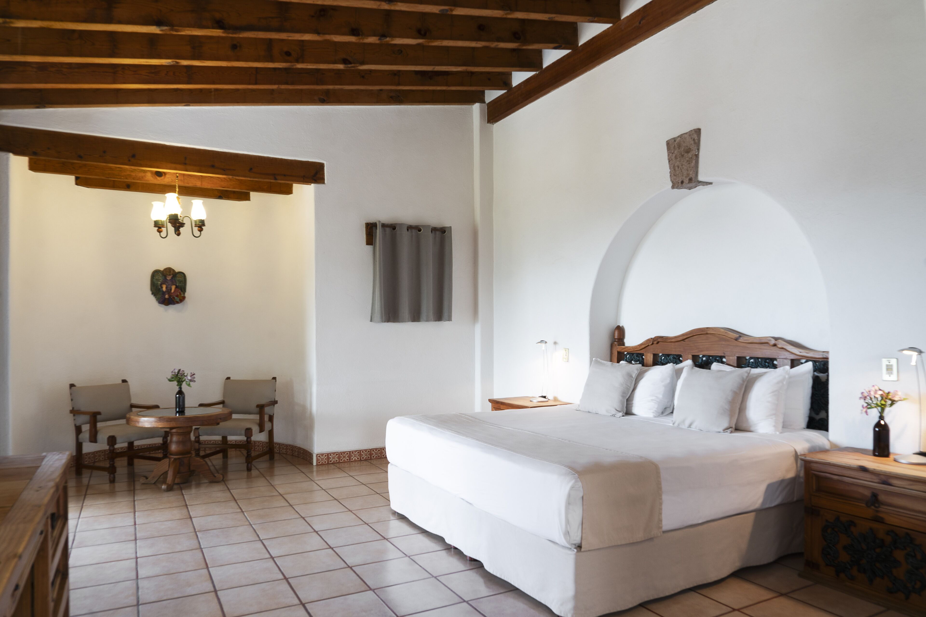 A bedroom with a large bed, a wooden ceiling, a dining table with chairs, and a chandelier.