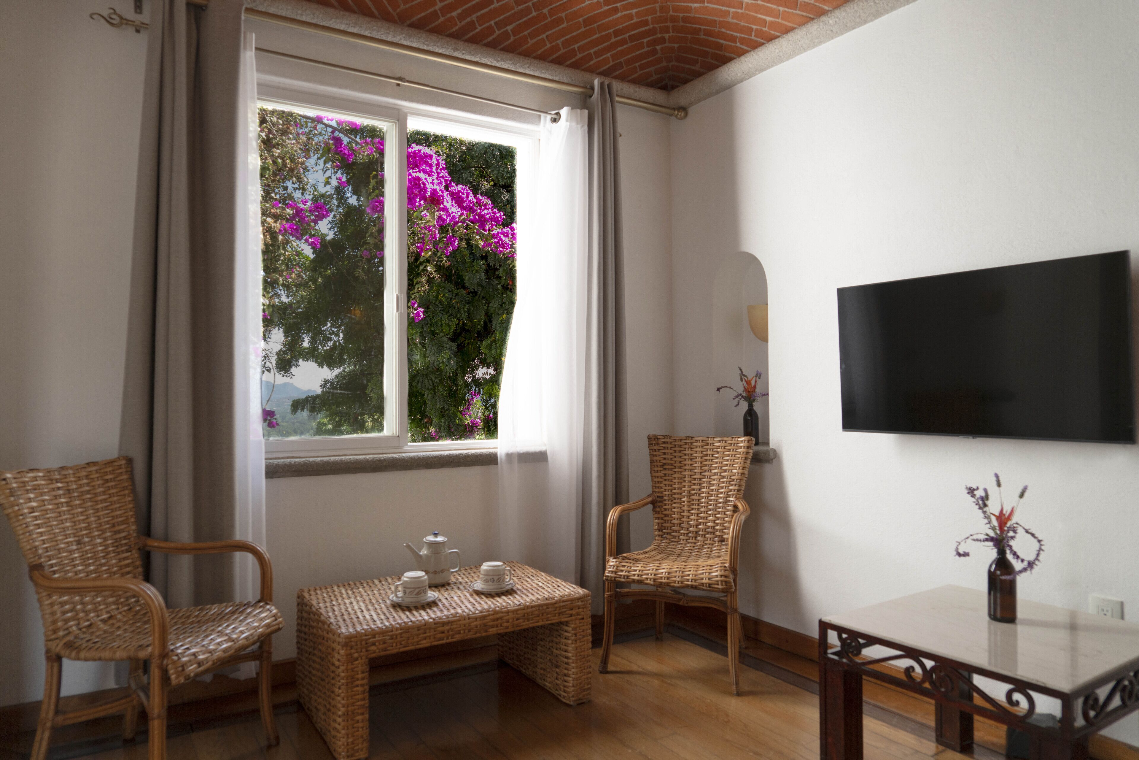 A room with a large window, wicker furniture, a flat-screen TV, and a small table with a vase.