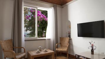 A room with a large window, wicker furniture, a flat-screen TV, and a small table with a vase.